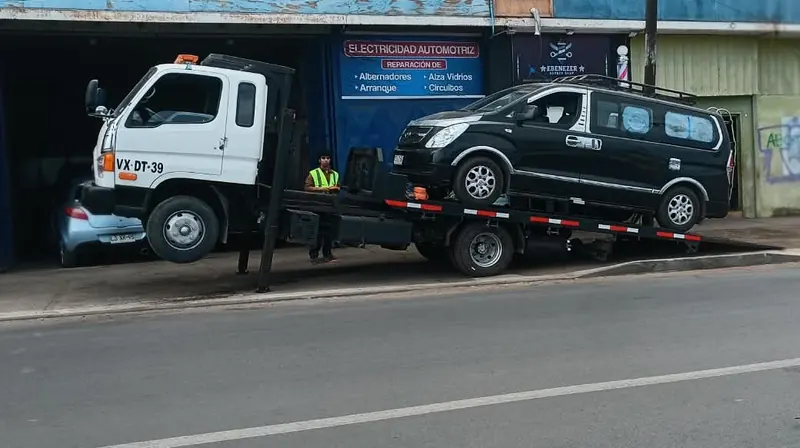 Furgón negro subido a la grúa Keeper frente a un taller de electricidad automotriz